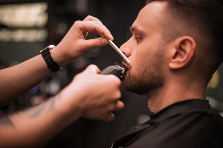 Close-up of a barber trimming a client's mustache with electric clippers and a comb, showcasing precise grooming technique