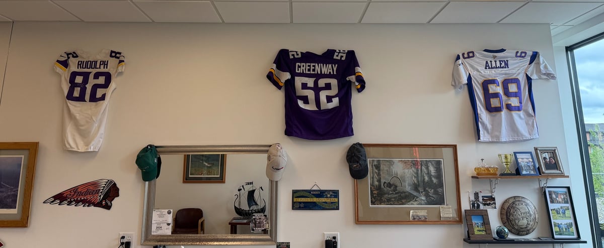 Three sports jerseys and memorabilia displayed on a beige wall with framed photos and collectibles below